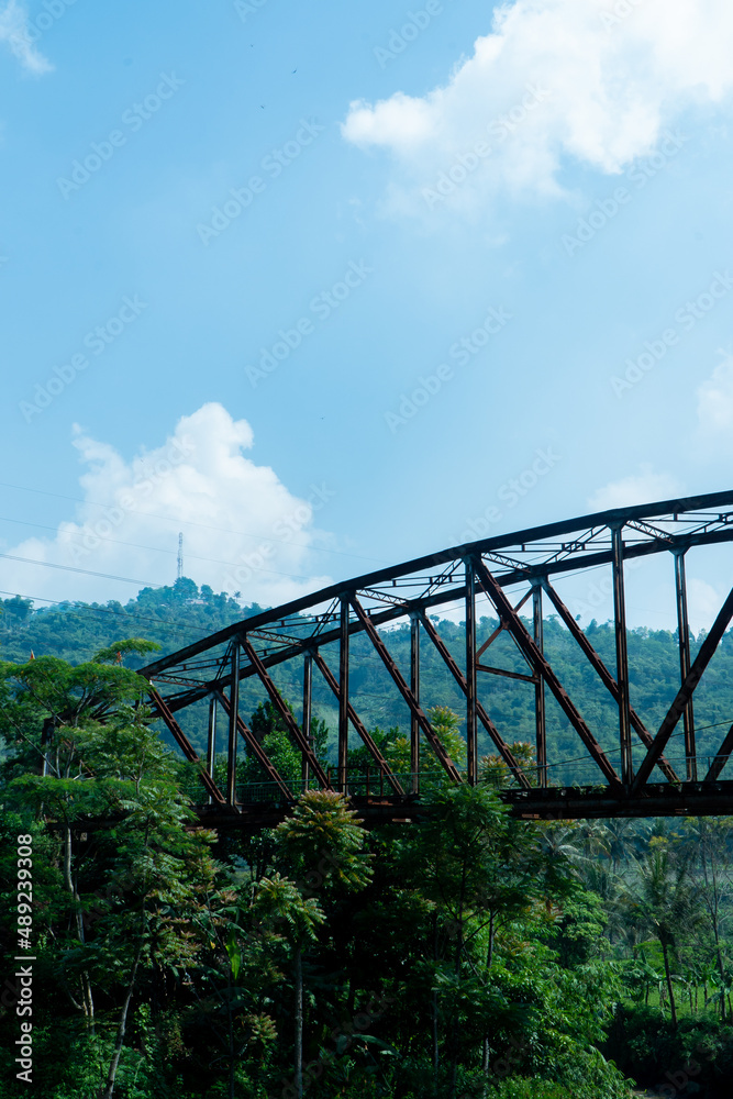 an old iron bridge in a village, with a view of a green forest an old iron bridge in a village, with a view of a green forest