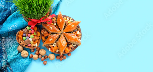 Nowruz festive table. arabic dessert baklava, sweets, nuts, dry fruits, green wheat grass on blue background. Spring equinox in March, Nowruz Holiday. top view. banner. copy space photo