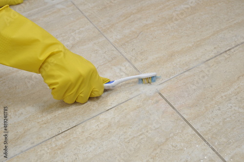 Cleaning tile joints with a toothbrush. Yellow household gloves. photo