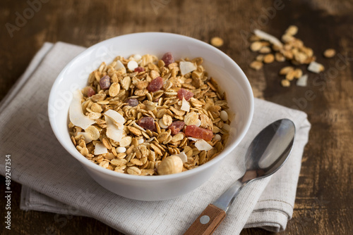A bowl of homemade granola on a wooden table with a spoon. Granola with nuts and dried fruits for a healthy breakfast. Close-up.