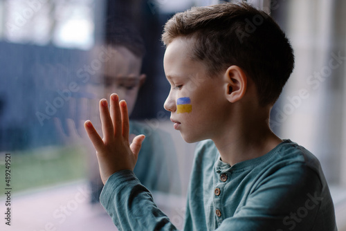 Fotografie, Obraz the child sits at the window with the flag of ukraine