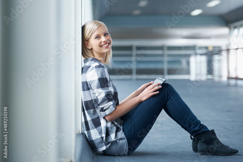 College can be the best years.... Shot of a young female student sitting against the wall in a university hall.