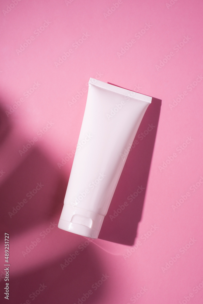 Plastic white tube for cream or lotion. Skin care or sunscreen cosmetic in top view on pink background with palm leaves shadow. Beauty concept for face care Plastic white tube for cream or lotion. Skin care or sunscreen cosmetic in top view on pink background with palm leaves shadow. Beauty concept for face care