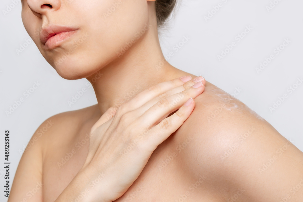 A cropped shot of a young caucasian woman massaging her body with her hands using a cream to moisturize the skin isolated on a gray background. Skin care A cropped shot of a young caucasian woman massaging her body with her hands using a cream to moisturize the skin isolated on a gray background. Skin care