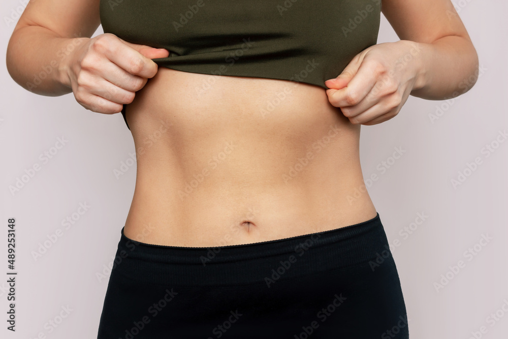 Cropped shot of a young slender woman with toned stomach with abs isolated  on a beige