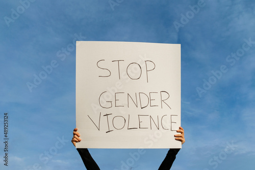 manos de mujer sujetando en alto una pancarta ,protestando contra la violencia de genero, escrito en lenguaje ingles, con el cielo de fondo.