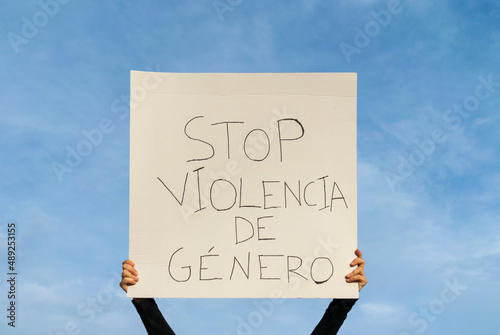 manos de mujer sujetando en alto una pancarta ,protestando contra la violencia de genero, escrito en lenguaje castellano, con el cielo de fondo.