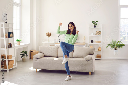 New home new life. Woman is very happy that she recently bought new house and it makes her feel on verge of happiness. Woman showing keys clenching fist of happiness while standing in new living room.