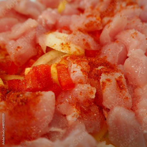 raw turkey meat cut into pieces sprinkled with red pepper, onion, potatoes before baking in the oven. side view