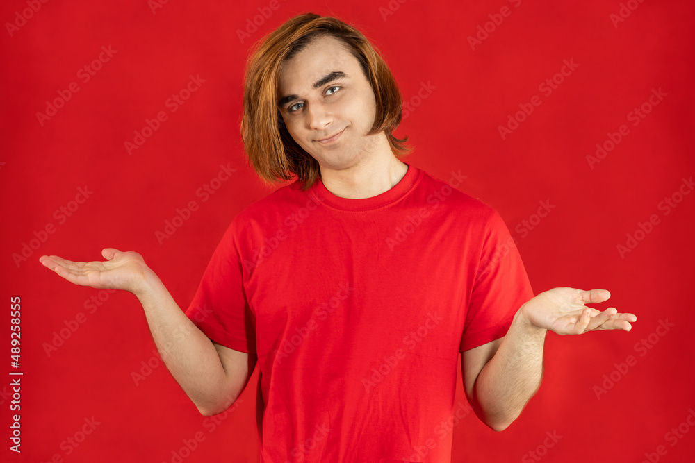 Young man Prep Student with long hair. Portrait of a guy spreading arms open with palms up on a red background Young man Prep Student with long hair. Portrait of a guy spreading arms open with palms up on a red background