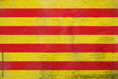 Full frame photo of a weathered flag of Catalonia painted on a plastered brick wall.