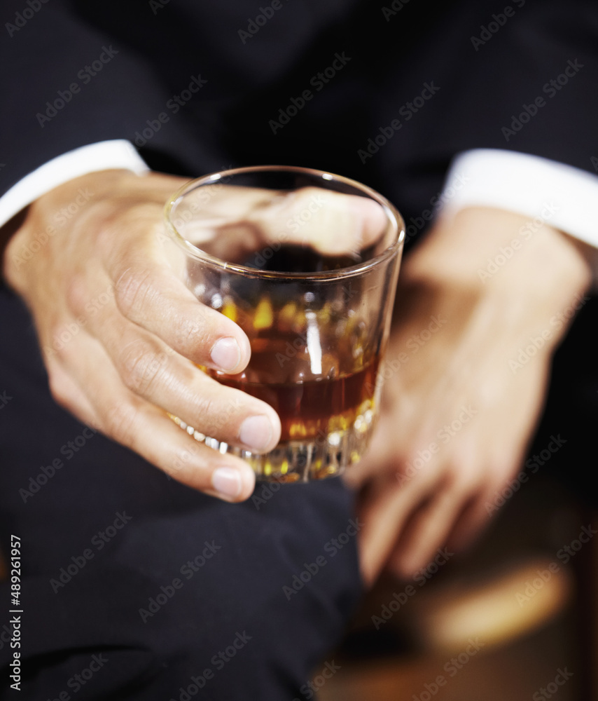 Its a mans world. Mans hand holding a whiskey glass balanced on his knee.