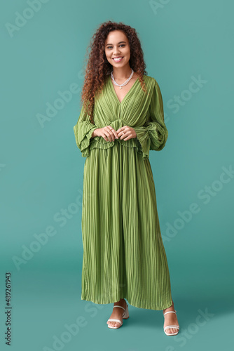 Fotografia Young African-American woman in dress with stylish jewelry on green background