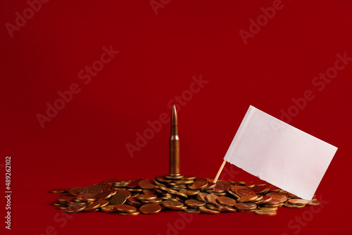 Live cartridge of a Kalashnikov assault rifle with an empty white flag on coins on a red background. The concept of military events and relations between countries. Copy space.
