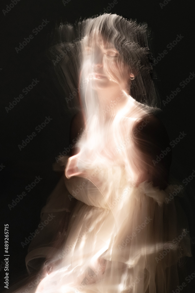 Abstract woman with beige dress and black hairs silhouette in bright light trails of light painting. Portrait in the style of light painting. Long exposure photo. Image contains noise and motion blur