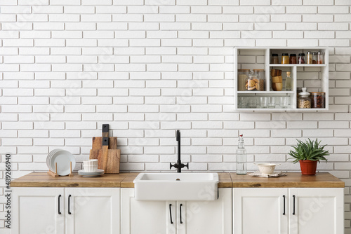 Counters with sink, kitchen utensils and shelving unit hanging on white brick wall