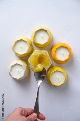 hold a spoon with honey in your hand on a white background, around scented candles made of soy wax. top view
