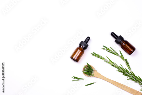 Aromatherapy herbal oil. Bottle glass with rosemary essential oil, wooden spoon, and fresh rosemary twig on white background.