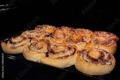 Twelve baked cinnamon buns on tray in electric oven. Swedish cuisine, homemade bakery, food, cooking and pastry concept