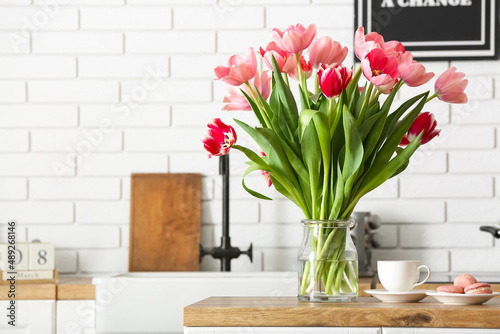 Beautiful tulips, cup and macarons on table in kitchen