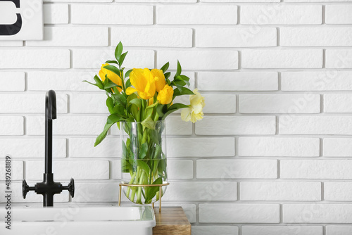 Vase with flowers on kitchen counter near white brick wall