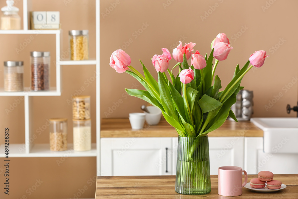 Vase with tulips, cup and macarons on wooden table in kitchen