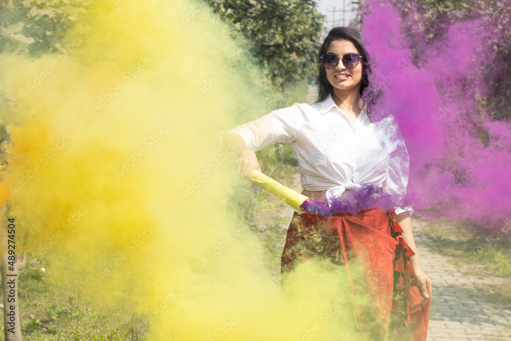 Beautiful young girl woman with Multicolored smoke bombs color cloud of dry color Holi powder colour gulal abeer event in spring break in the park Holi festival of color