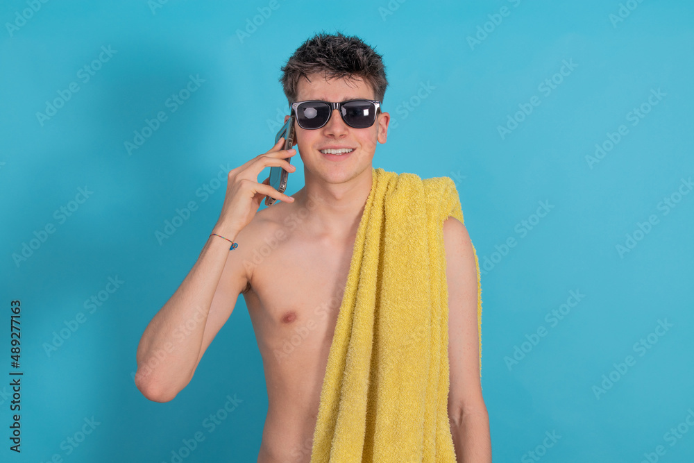 young male teenager with mobile phone towel and sunglasses isolated on blue color background