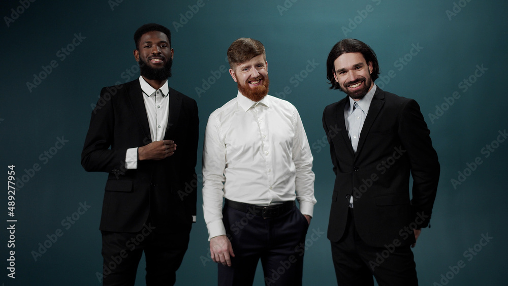 Three men friends in tuxedos are posing, smiling and looking at the camera funny Three men friends in tuxedos are posing, smiling and looking at the camera funny