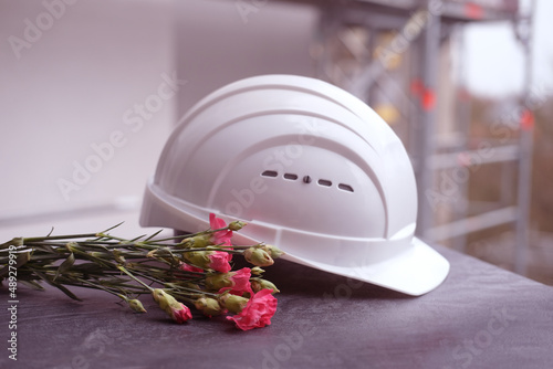 white hardhat, red carnations, helmet on background of buildings, protection inspecting at construction site, symbol of builder's death, day of mourning, civil engineering concept, builder's day