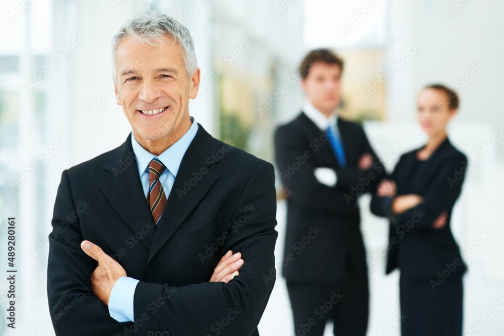Leading them to great success. Portrait of a mature businessman with colleagues standing in the background. Leading them to great success. Portrait of a mature businessman with colleagues standing in the background.