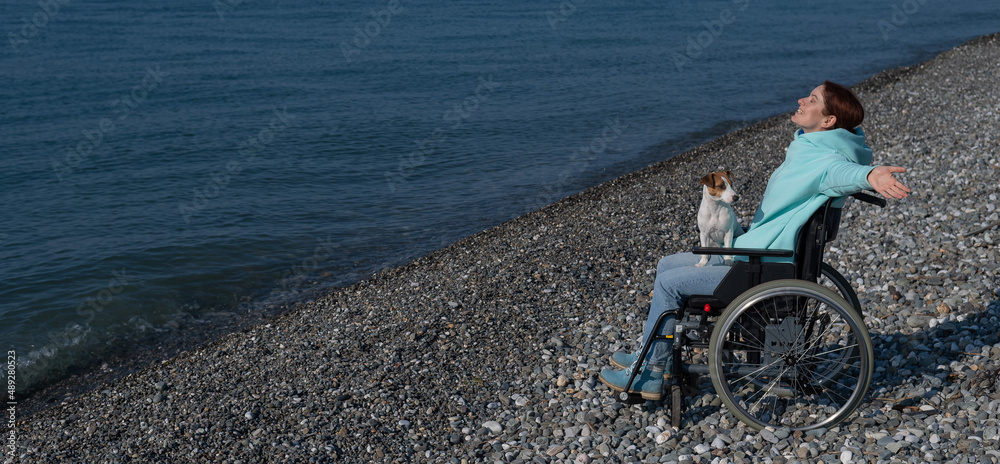 Fototapeta premium Happy woman in a wheelchair on the seashore raised her hands and imagines that she is flying. 