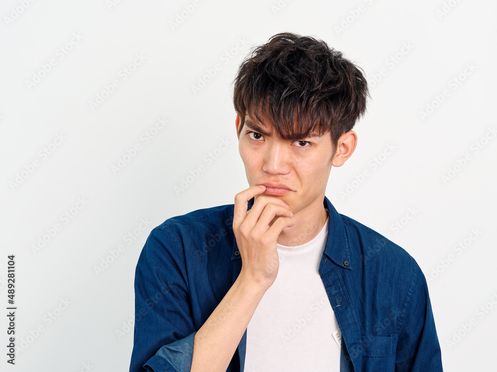 Portrait of handsome Chinese young man with curly black hair in blue shirt posing against white wall background. Hand on his mouth with disgusted expression, looks unhappy, front view. Portrait of handsome Chinese young man with curly black hair in blue shirt posing against white wall background. Hand on his mouth with disgusted expression, looks unhappy, front view.