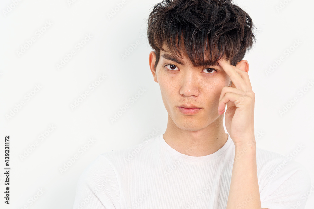 Portrait of handsome Chinese young man with curly black hair in white T-shirt posing against white wall background. Fingers on head and looking at camera, looks seriously, close up front view. Portrait of handsome Chinese young man with curly black hair in white T-shirt posing against white wall background. Fingers on head and looking at camera, looks seriously, close up front view.