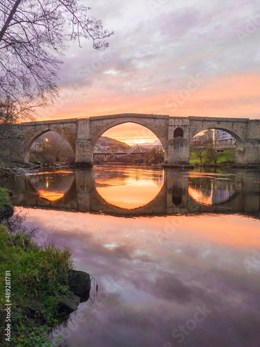 Roman bridge of Ourense reflected in the Miño river in a beautiful sunset.