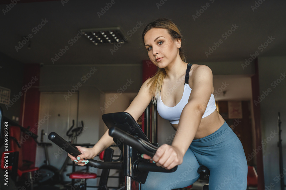 Fototapeta premium one woman young adult female training at the gym in day sitting riding on the spinning bike bicycle cardio workout exercise real people copy space