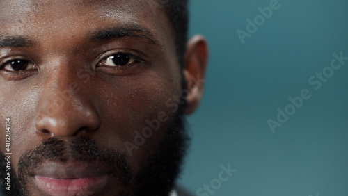 A young black bearded man in a official suit blinks and looks at the camera
