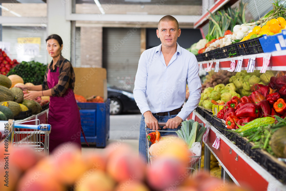 Obraz premium European man shopping in greengrocery. Asian woman in uniform working in salesroom.