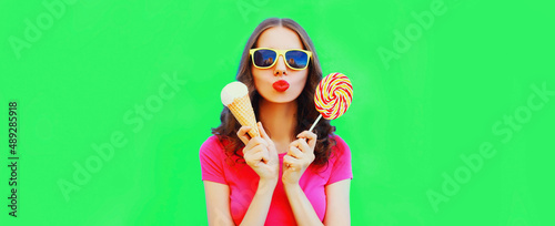 Portrait of happy young woman with ice cream blowing her lips on green background