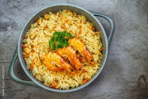 Rice with shrimps in a frying pan on a wooden table, top view.