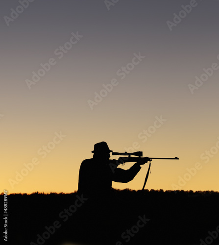 Preparing to shoot. A silhouette of a man in the outdoors holding up his sniper rifle.