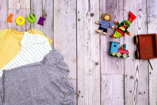 yellow bodysuit, gray bodysuit and green bodysuit made of cotton with a child's toys. Clothes for newborns on grey background. Flat lay,