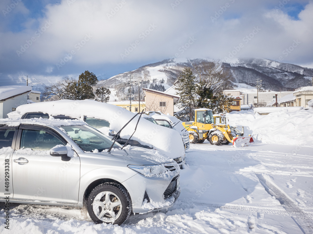 parking snow-covered cars and yellow snowplow vehicles in the parking lot