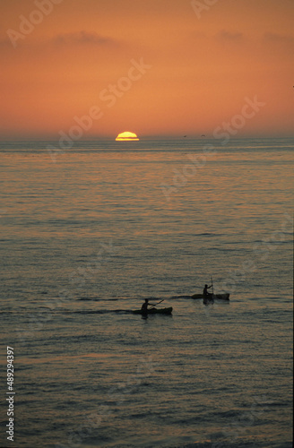Two kayaks paddle by as sunsets off California coast