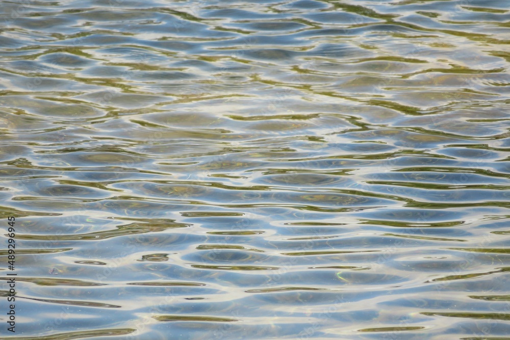 Ripples and sun reflection on light blue water river surface, natural background