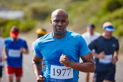 Feeling strong and invincible on the road. Shot of a young man running a marathon with other runners in the background.