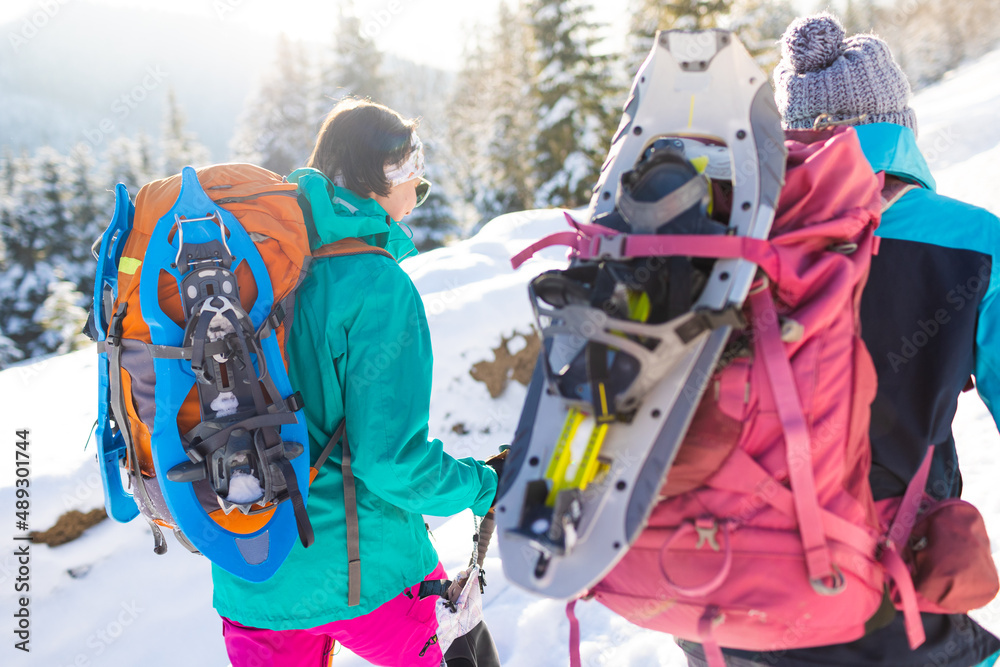 Two women walk with snowshoes on the backpacks, winter trekking