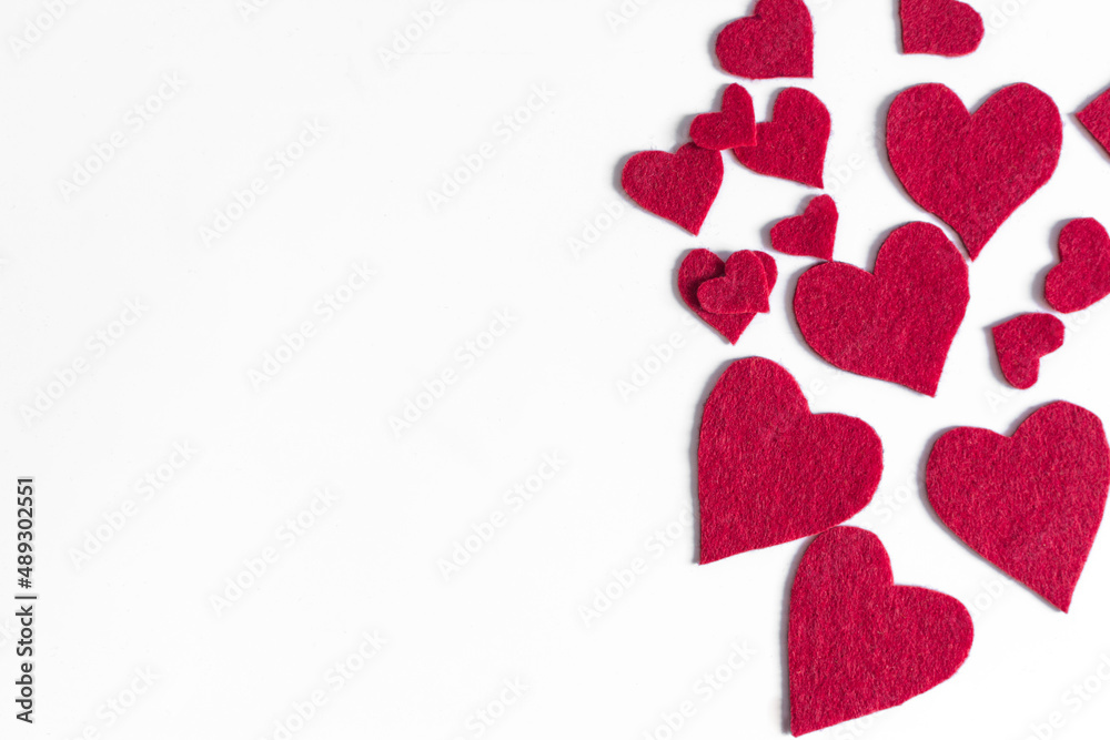 Romantic background of a scattering of bright red fabric hearts on a white background of copy space.