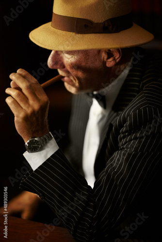 Lighting up. Aged mob boss wearing a hat and looking serious while lighting up a cigarette. photo