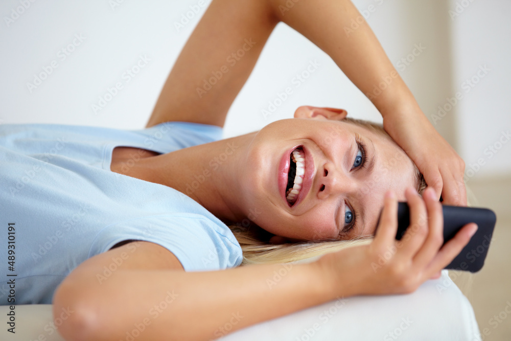 Thats hilarious. Young woman lying on the sofa at home and sending a text using her mobile. Thats hilarious. Young woman lying on the sofa at home and sending a text using her mobile.